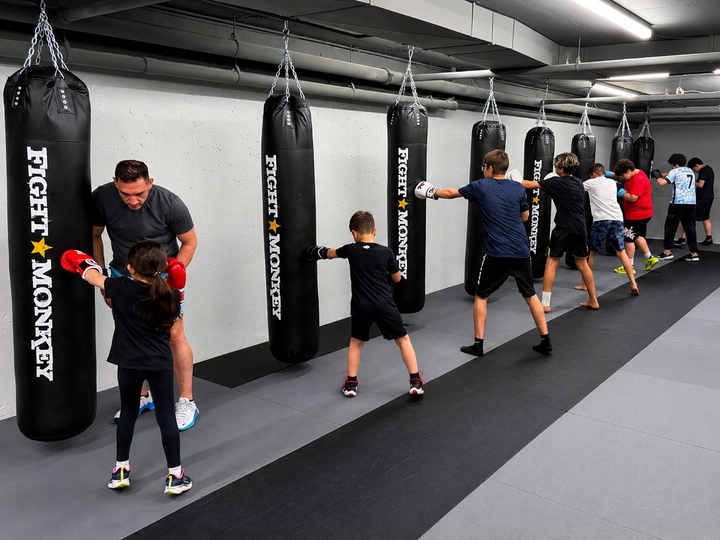 Coach leading a kids boxing class on the heavy bags at DKM Academy